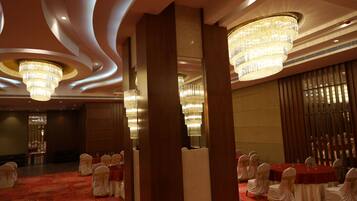 A banquet hall with round tables, white chairs, and chandeliers.