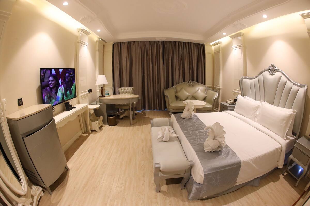 A hotel room with a large bed, a desk with a chair, a television, and a window with curtains.