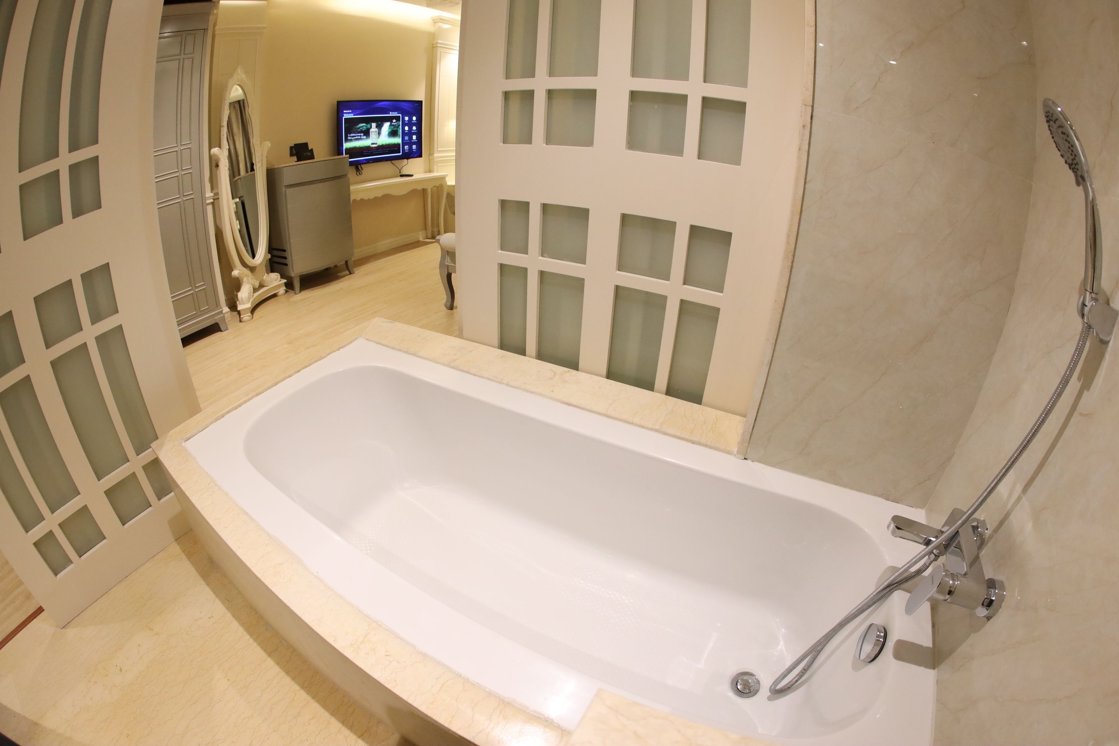Un baño moderno con una bañera grande, un tocador con espejo y un televisor al fondo.