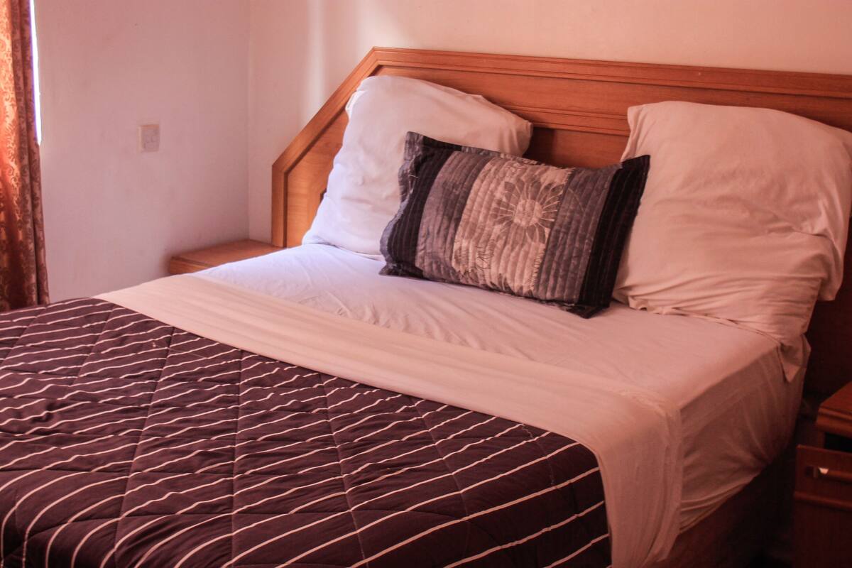 Cama bem arrumada com roupa de cama listrada, cabeceira de madeira e duas almofadas.