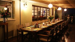 Una larga mesa de comedor dispuesta para una comida en una habitación con sillas de madera y techo alto.