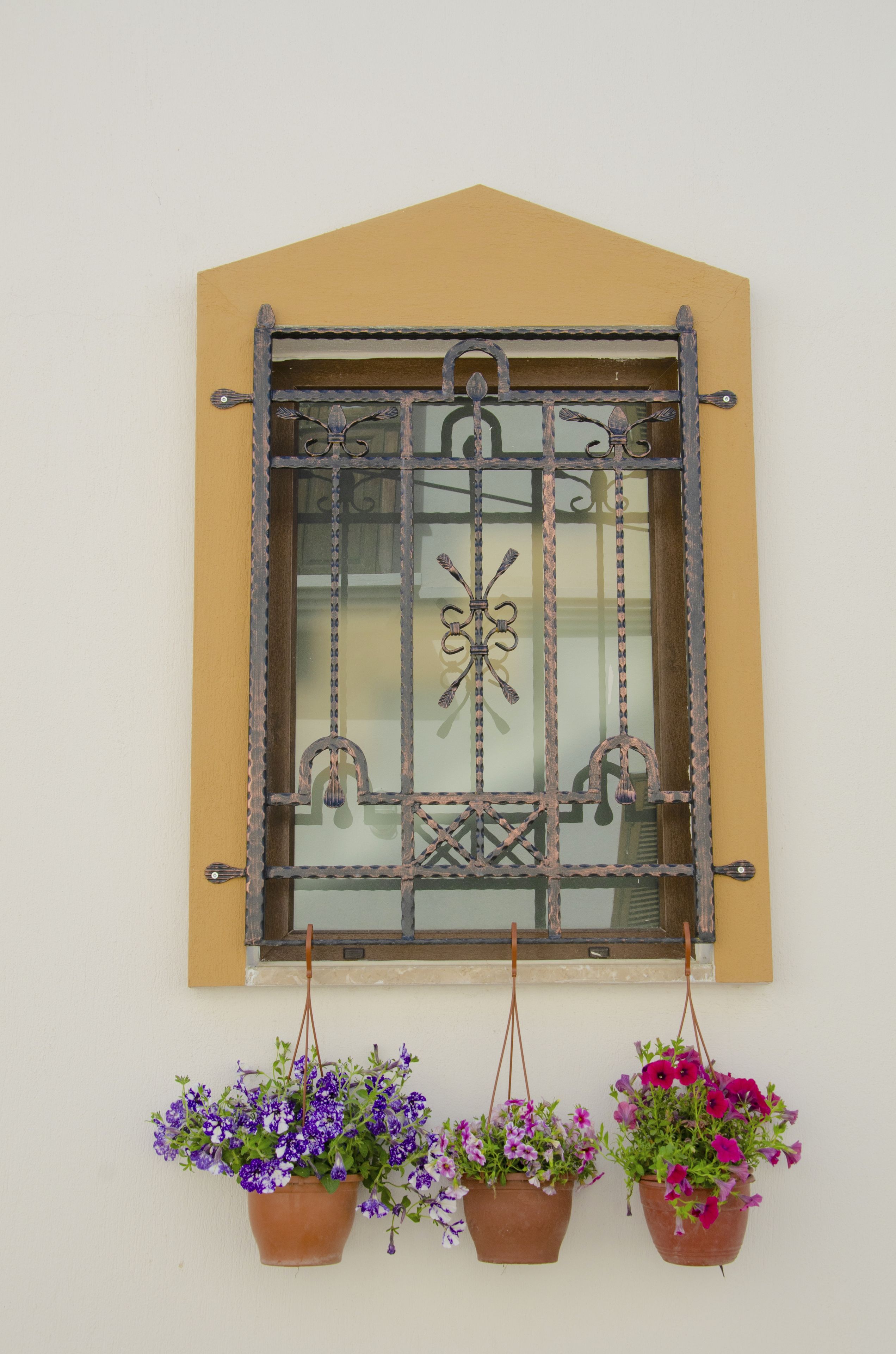 A window with a decorative metal grille and three hanging flower pots below it.