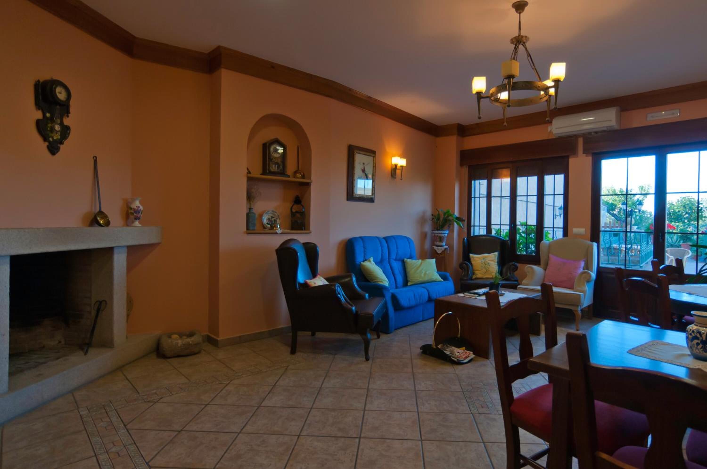 Una sala de estar con chimenea, un sofá azul, una mesa de comedor con sillas y ventanas amplias.