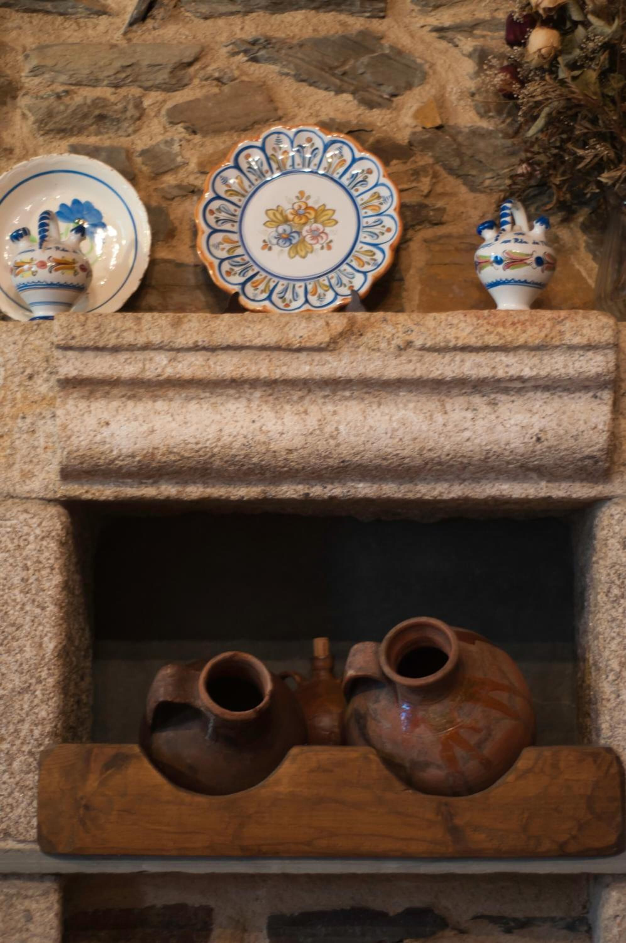 A stone fireplace with two pottery pieces and a decorative plate.