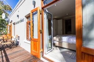 A modern hotel room with a wooden door, a bed, and a small seating area with a table and chairs outside.