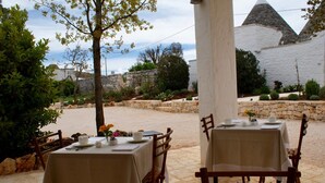 An outdoor dining area with tables set for two, surrounded by stone walls and greenery. - Masseria Grofoleo (Locorotondo)