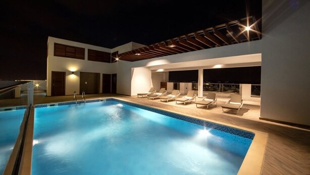 Un área de piscina en la azotea con sillones de descanso y una pérgola.