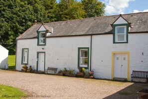 A white building with green trim, a bench, and potted plants in front. - Kirkwood Holiday Cottages (Lockerbie)