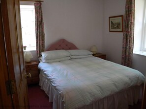 A bedroom with a bed, a nightstand, a lamp, and a window with curtains. - Kirkwood Holiday Cottages (Lockerbie)