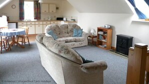 A cozy living room with a sofa, a dining table with chairs, a kitchen area, and a fireplace. - Kirkwood Holiday Cottages (Lockerbie)