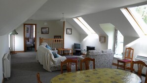 A cozy attic room with a dining table, chairs, a sofa, and a TV. - Kirkwood Holiday Cottages (Lockerbie)