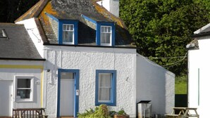 A white cottage with blue trim, a small front porch, and a bench. - Kirkwood Holiday Cottages (Lockerbie)