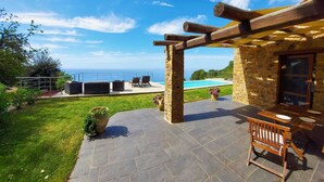 Un patio de piedra con piscina, mobiliario exterior y vistas al mar.
