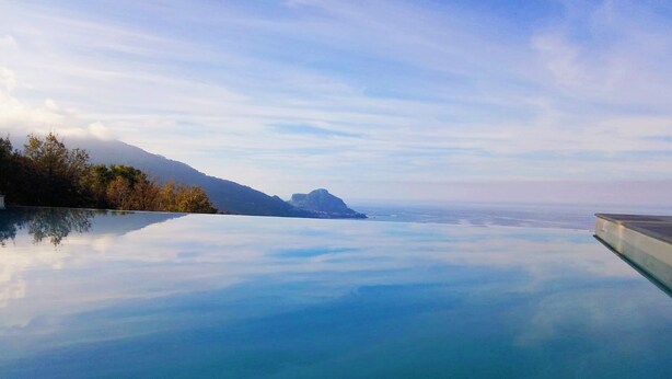 Piscina infinita de color azul intenso con vistas a montañas lejanas y un cielo despejado.