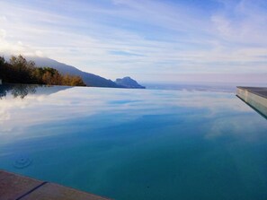 Piscina infinita de color azul intenso con vistas a montañas lejanas y un cielo despejado.