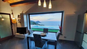 Una cocina moderna con un amplio ventanal que ofrece una vista panorámica del océano, una zona de comedor con mesa y sillas, y un televisor empotrado.
