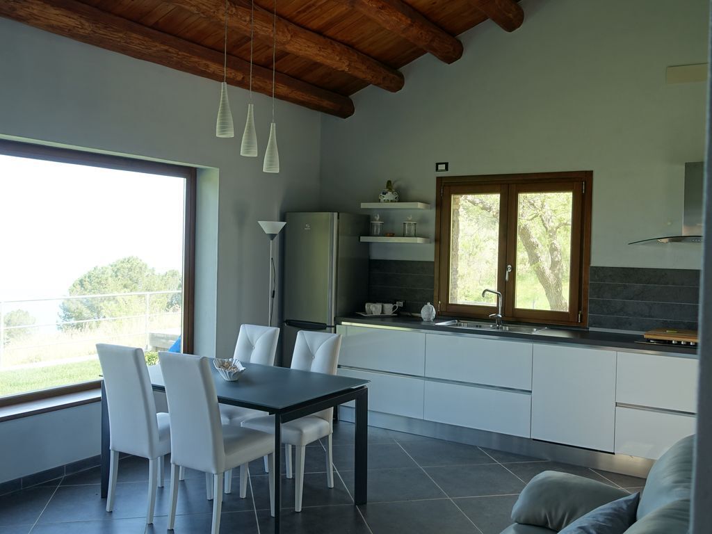 A modern kitchen with white cabinets, a dining table with chairs, and a large window.