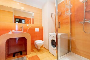 A bathroom with a sink, toilet, washing machine, and a glass-enclosed shower area.