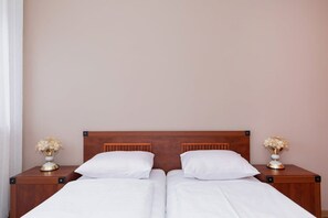 A double bed with white linens, two nightstands with flower vases, and a wooden headboard.