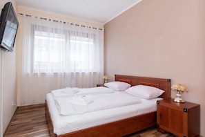 Ein Hotelzimmer mit einem hölzernen Bett, weißen Laken, einem Nachttisch mit einer Vase und einem an der Wand montierten Fernseher.