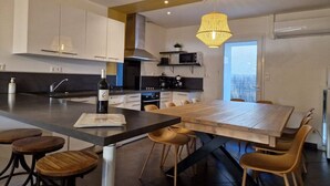 A modern kitchen with a large island, bar stools, and a dining table. - Loft Nature Bien-être Piscine Chauffée Privée Tarn (Peyrole)