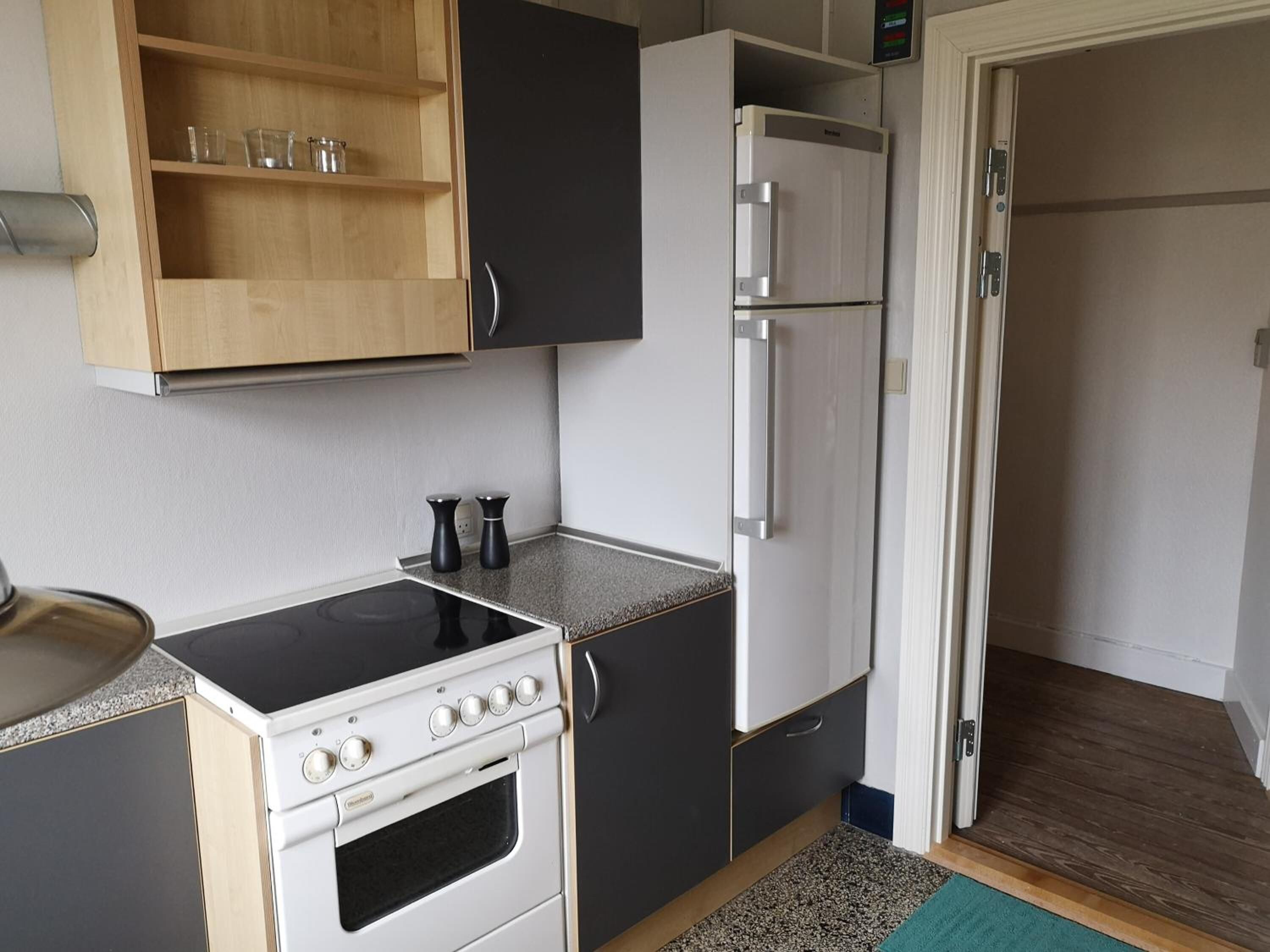 Une cuisine de taille réduite, équipée d’une cuisinière, d’un four, d’un réfrigérateur et de meubles de rangement en bois.