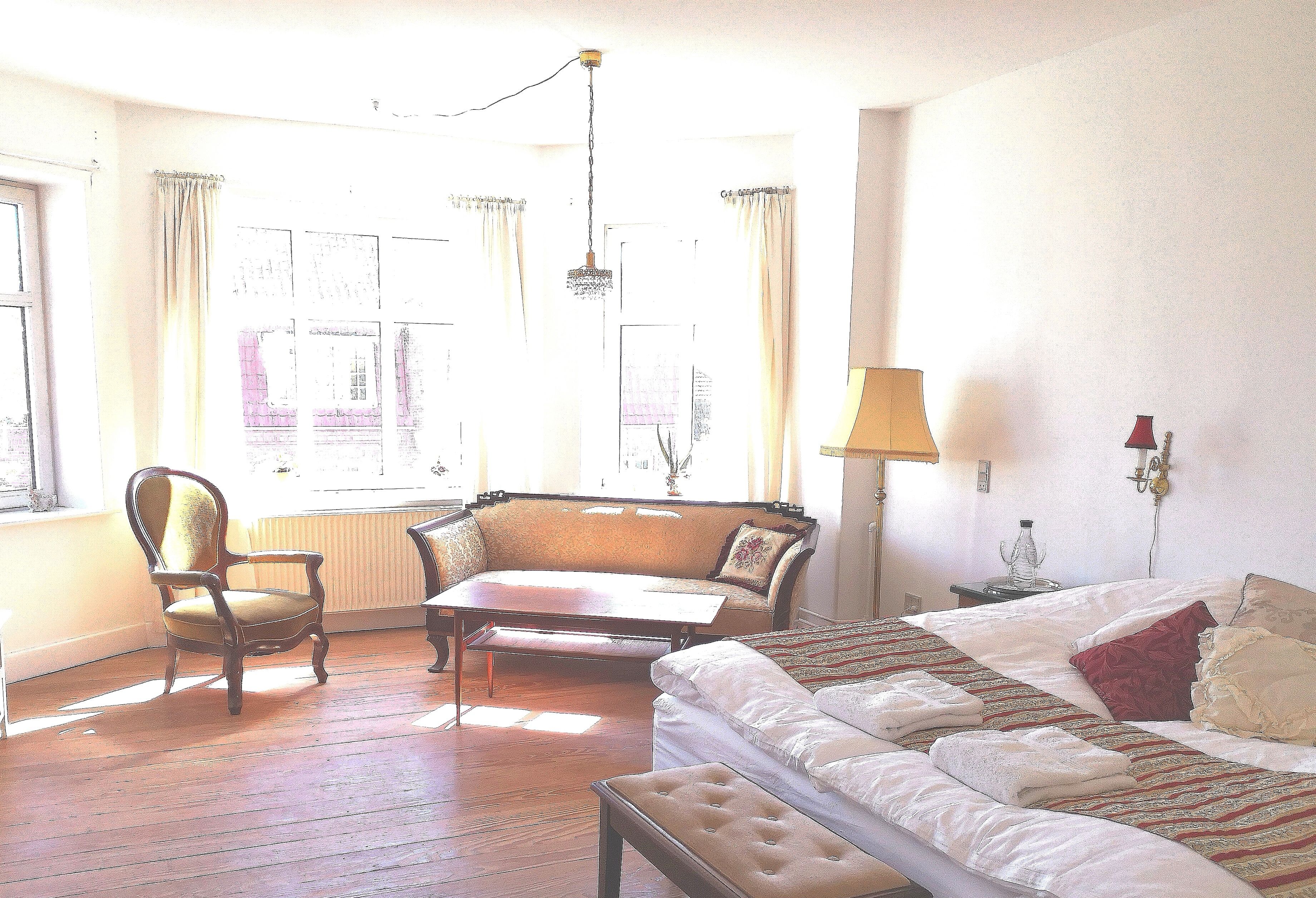A room with a bed, a sofa, a chair, a table, and a lamp.