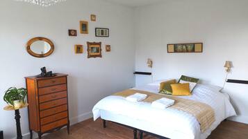 A bedroom with a wooden dresser, a bed with white bedding and multiple pillows, a chandelier, and several framed pictures on the wall.