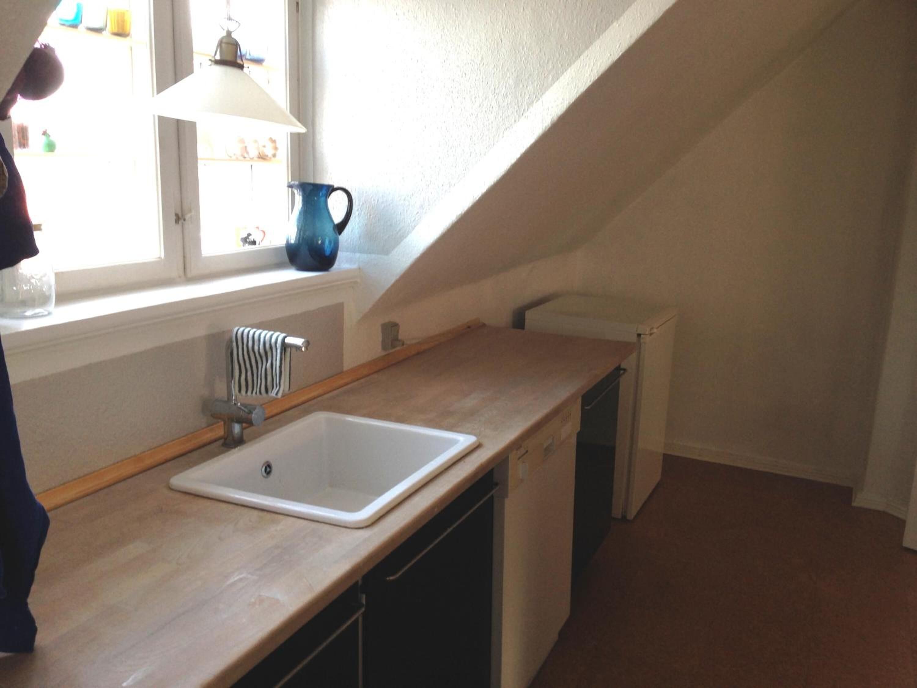 Eine kleine Küche mit Spüle, Fenster und Lampe.
