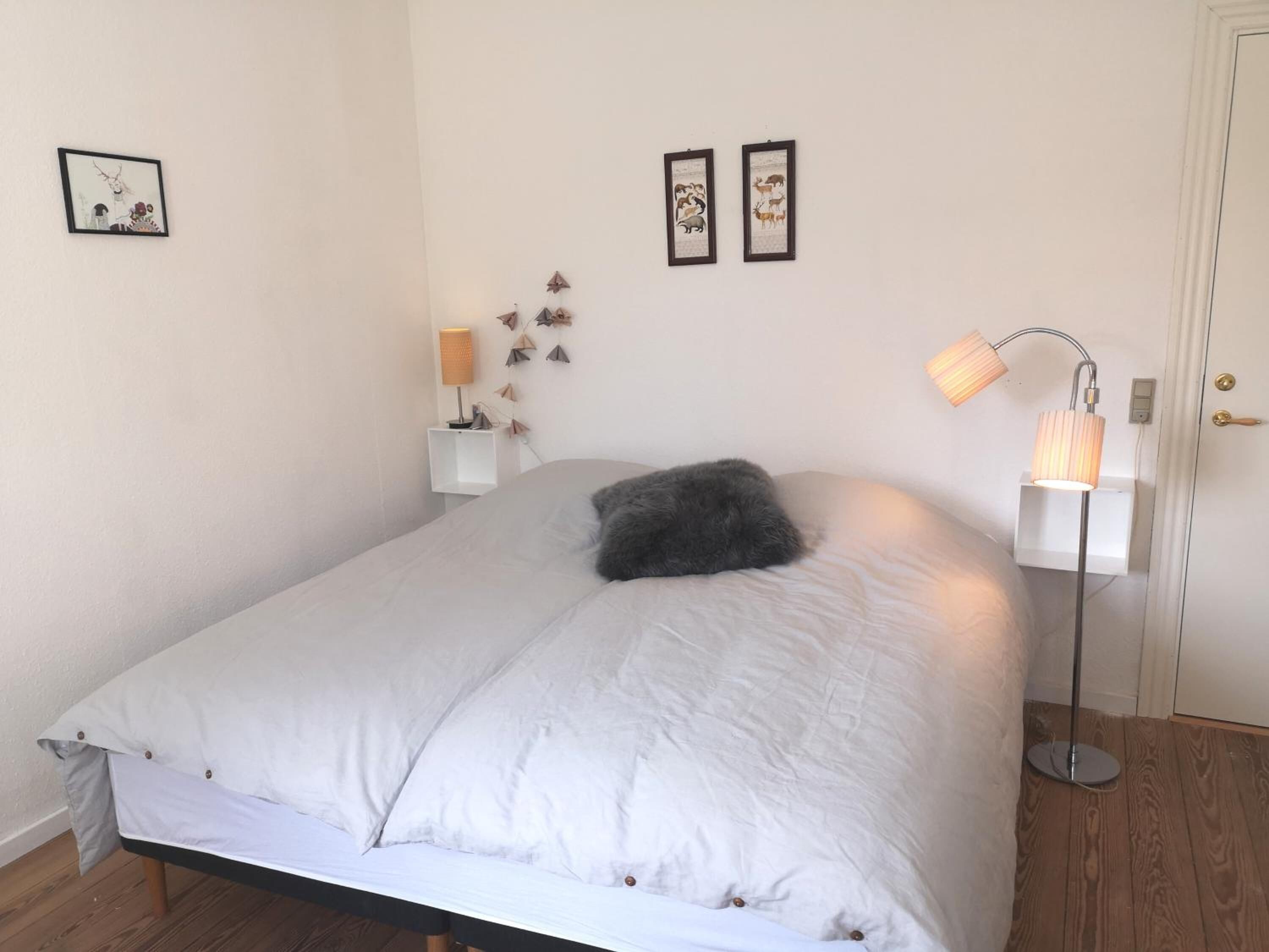 Ein Schlafzimmer mit Bett, Nachttisch, Lampe und Wandbildern.