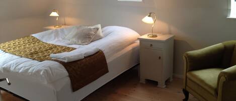 A bedroom with a bed, two bedside tables with lamps, a chair, and a skylight.