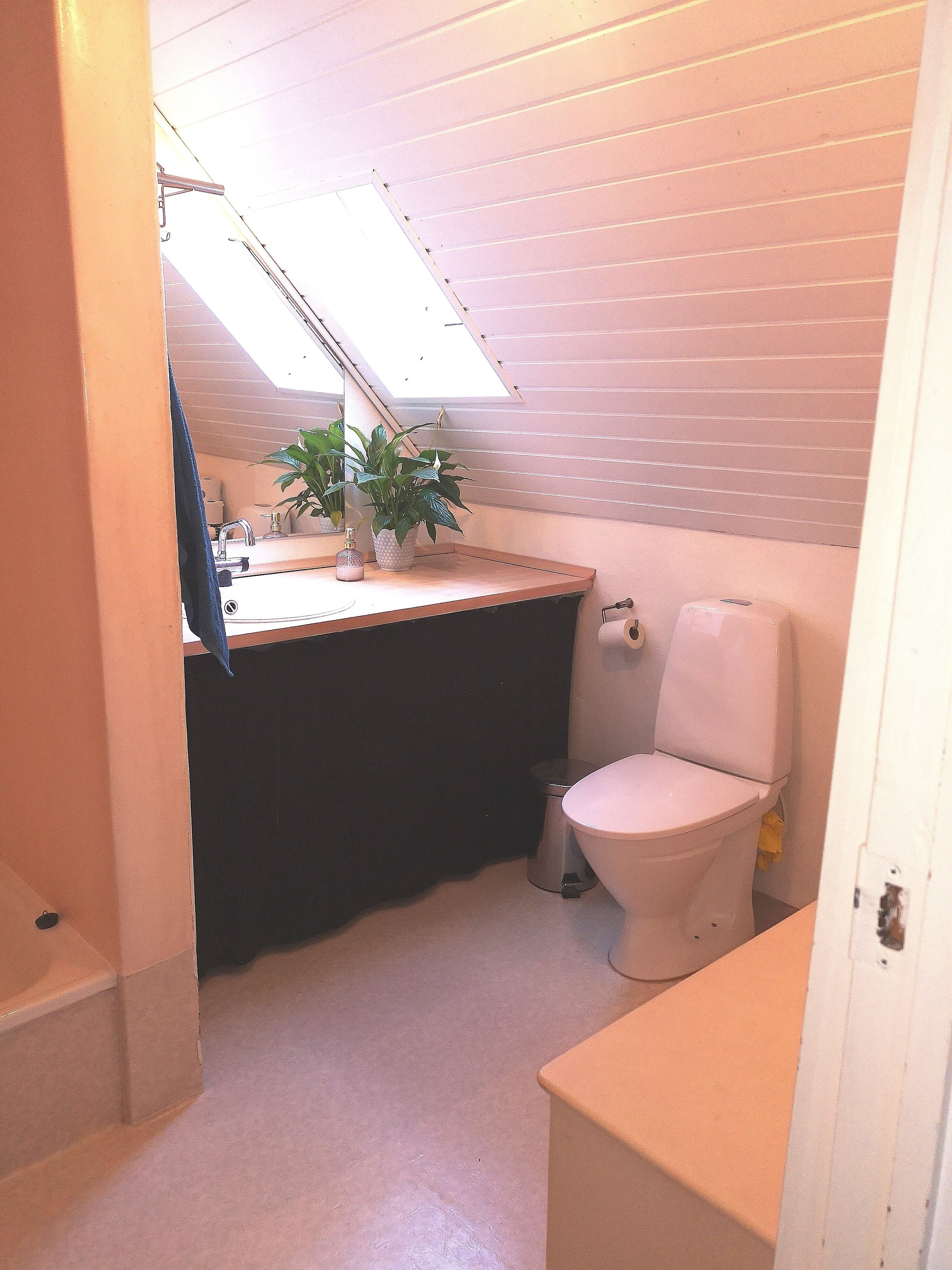 A small, compact bathroom with a skylight, a sink, a toilet, and a trash can.