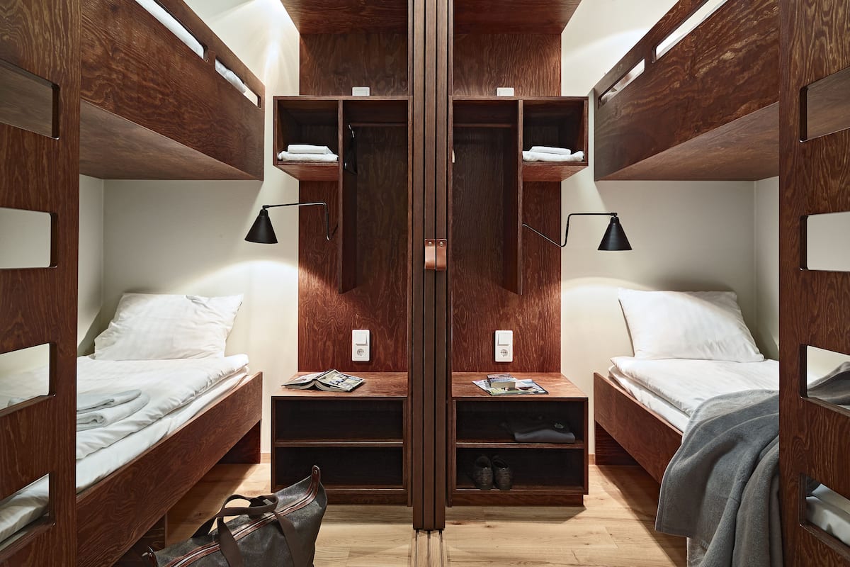 Una habitación pequeña y de madera con literas, estanterías integradas y lámparas de noche.