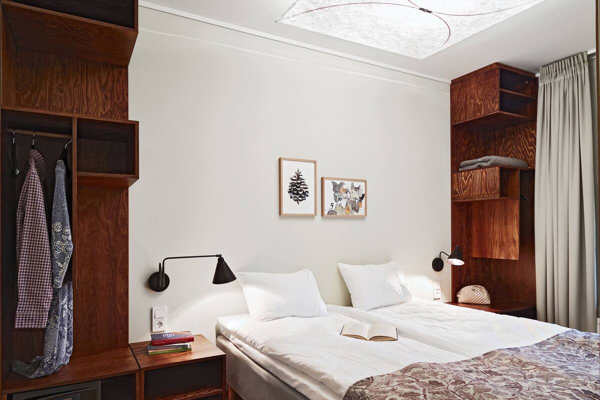 Una habitación de hotel con cama, mesitas de noche, armario y una obra de arte en la pared.