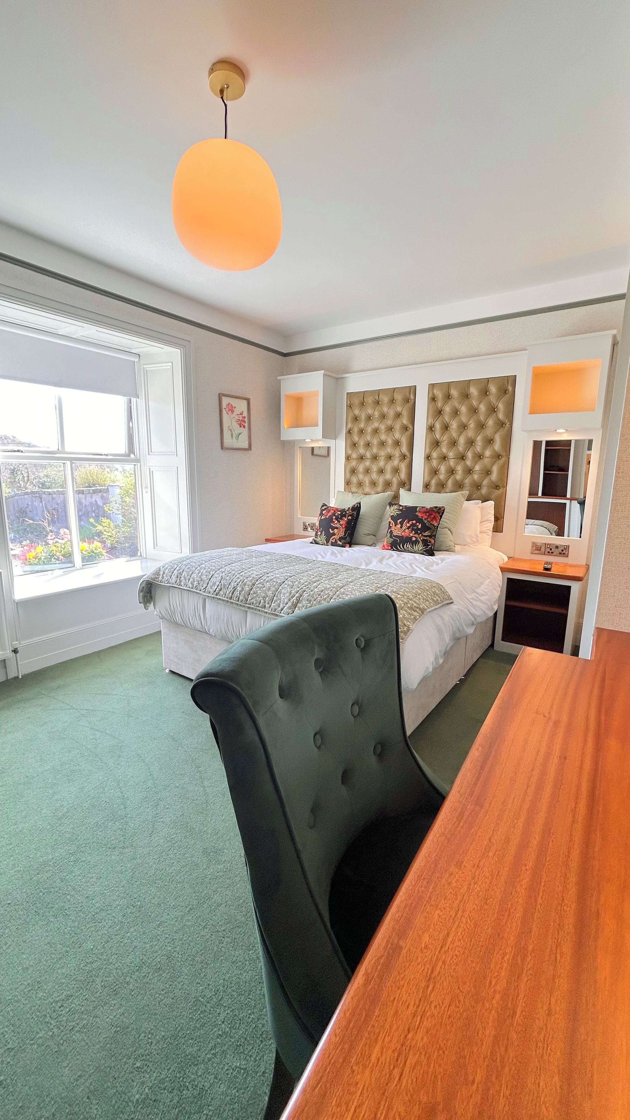 A hotel room with a bed, a desk, a chair, a window, and a ceiling light.