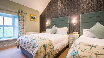 A hotel room with two beds, a window with curtains, a wall with a tree pattern, and a nightstand with a lamp.