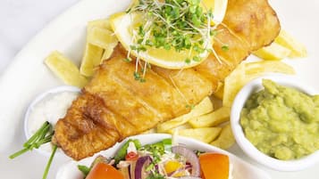 A plate of fish and chips with lemon wedges, sprouts, and a side of mushy peas and tartar sauce.