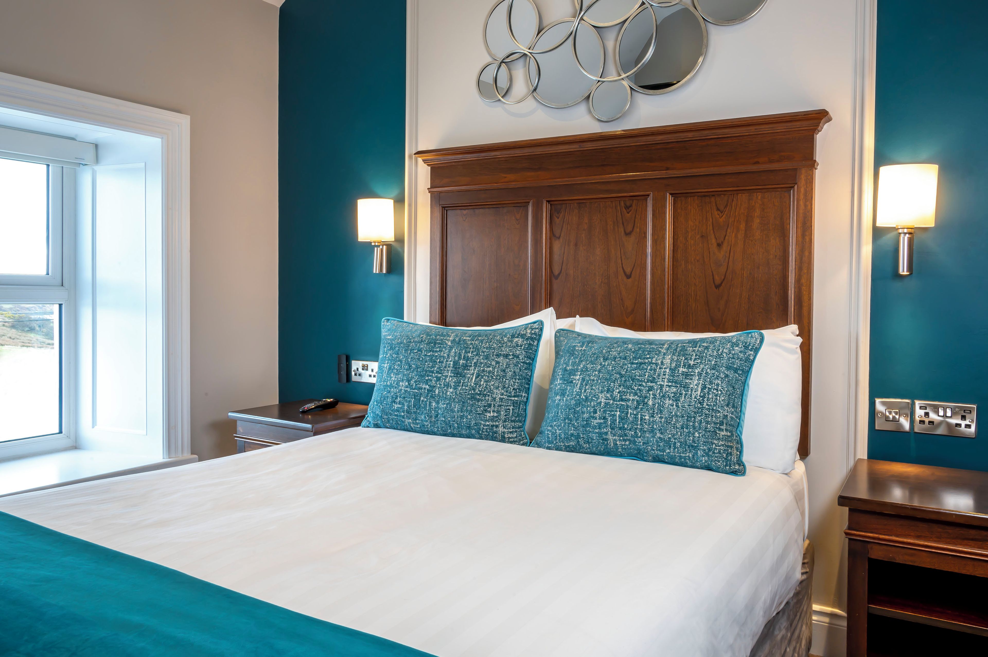 A hotel room with a large bed, two bedside lamps, a wooden headboard, and a view of the outdoors through a window.
