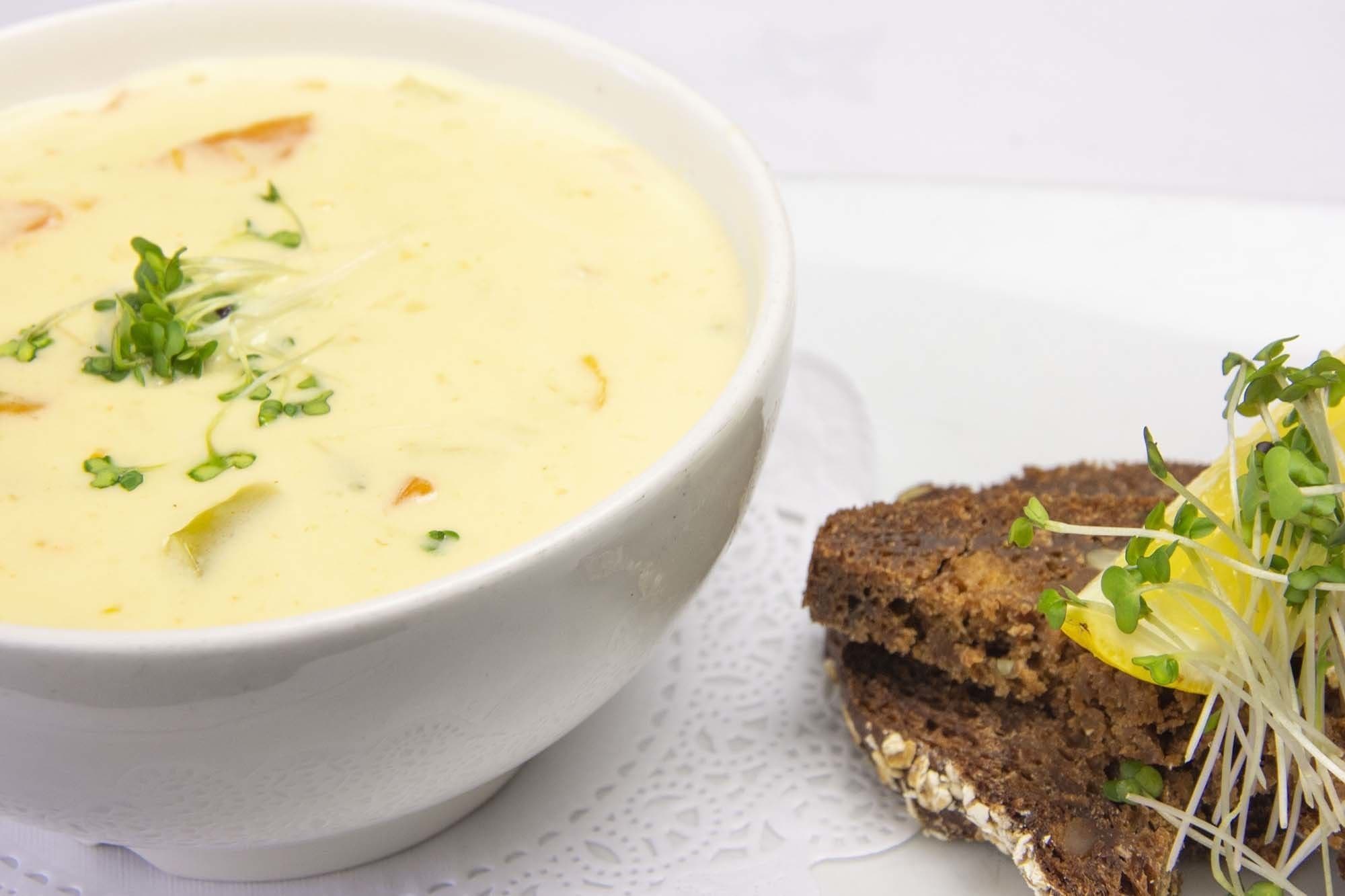A bowl of creamy soup garnished with green sprouts, accompanied by a slice of dark bread with sprouts and a lemon wedge.