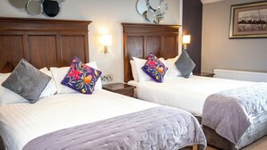 A hotel room with two beds, each with a headboard, a nightstand, a lamp, and a wall-mounted mirror. - Nevins Inn (Newport)