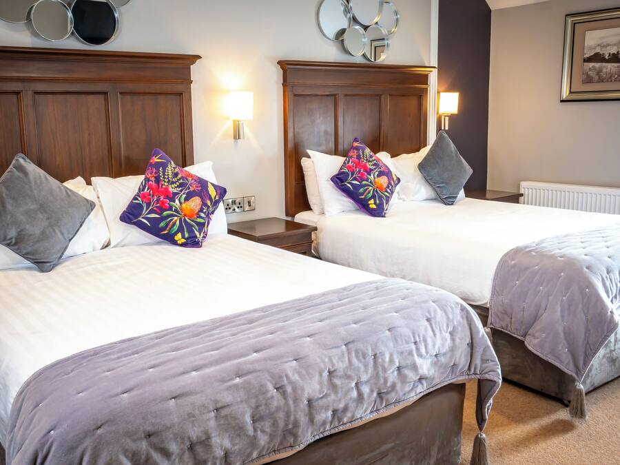 A hotel room with two beds, each with a headboard, a nightstand, a lamp, and a wall-mounted mirror.