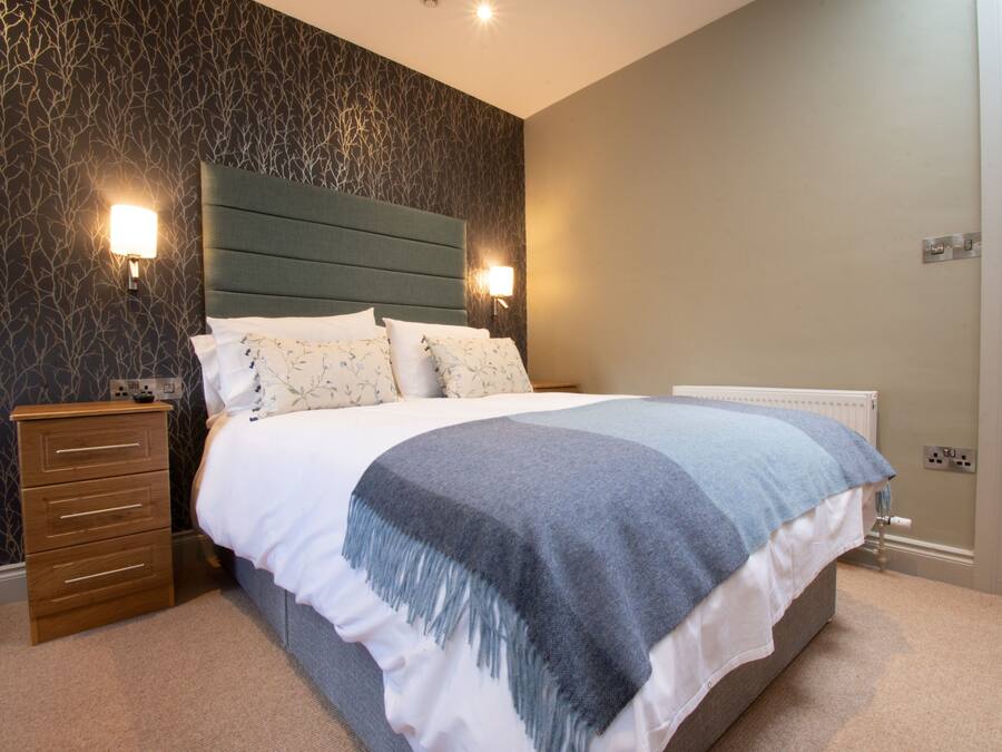 A bedroom with a bed, nightstands, a dresser, and a wall-mounted light fixture.