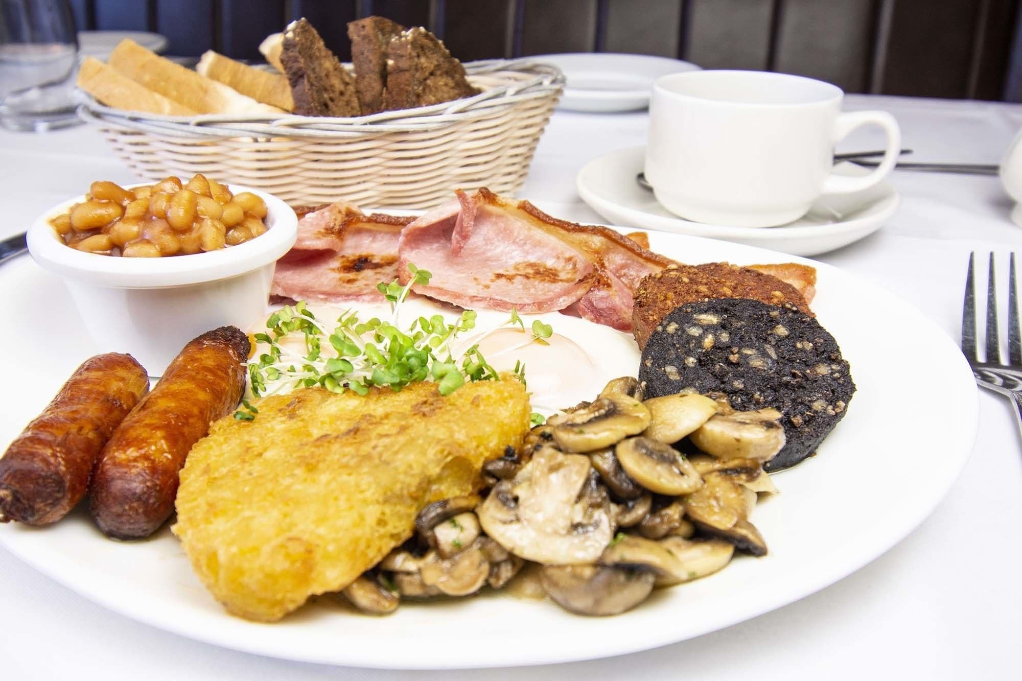 A breakfast plate with sausages, mushrooms, black pudding, bacon, beans, and toast.