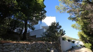 A white building with a stone wall in front, surrounded by trees. - Studio apartment GIRO (Omis)