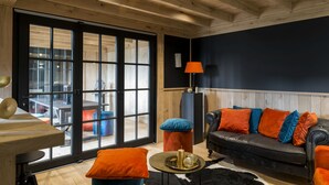 A cozy living room with a black leather sofa, orange cushions, a round coffee table, and a large window with a view of the outside. - B&B Bertem Natuur (Bertem)