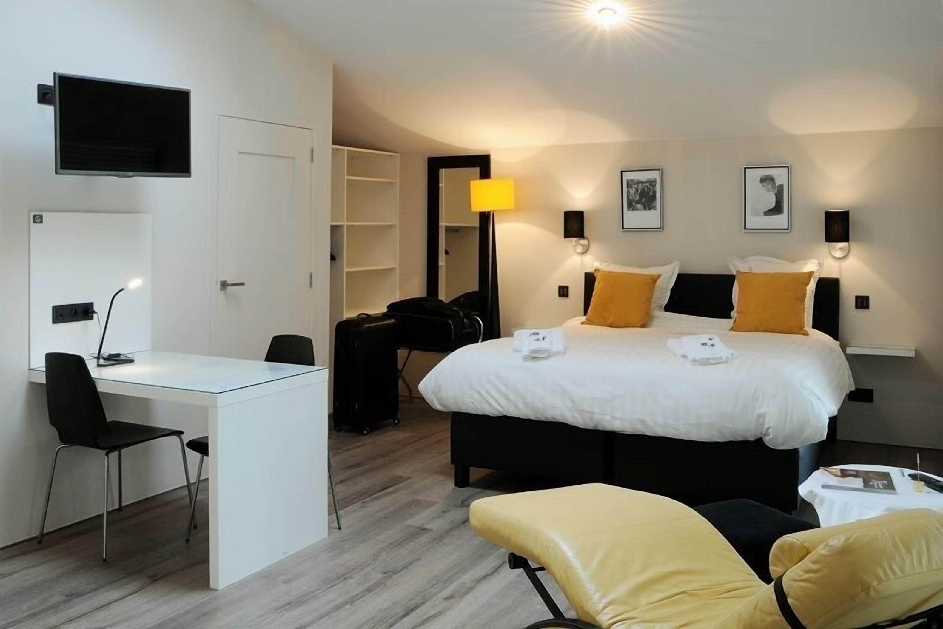 Una habitación de hotel con cama, escritorio, silla, televisor y espejo.