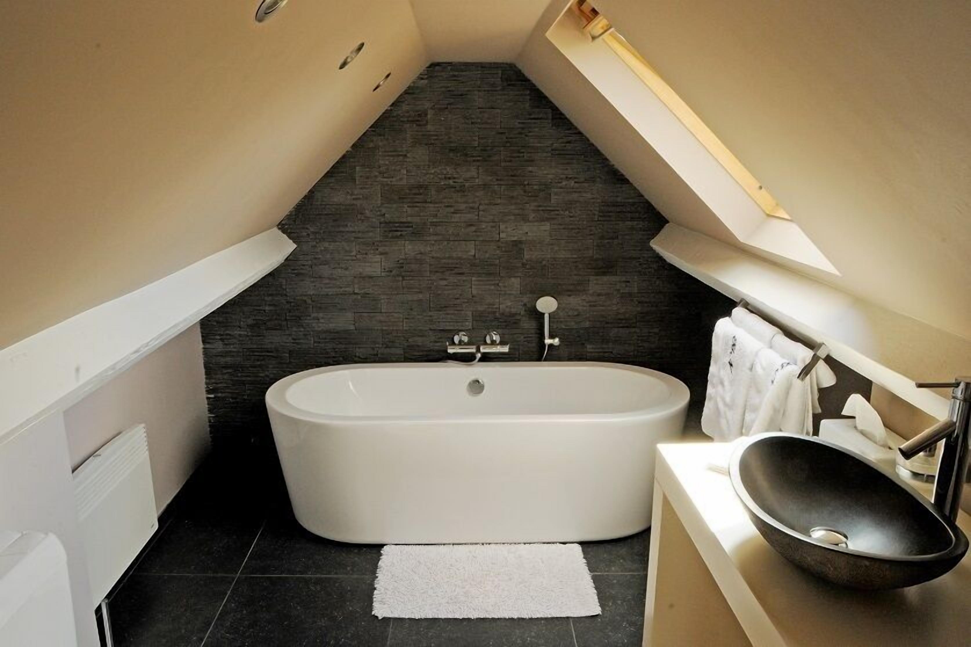 Une salle de bain moderne avec une baignoire sur pieds, un lavabo posé et un sol carrelé foncé.