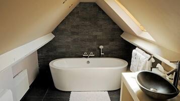 Une salle de bain moderne avec une baignoire sur pieds, un lavabo posé et un sol carrelé foncé.