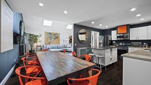 A modern kitchen with a central island, stainless steel appliances, and bright orange chairs around a wooden table. - Huge Backyard, Large Living Room with Dining Area, Large Den with Built-In... (Southampton)
