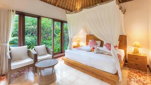 Un dormitorio amplio con una cama grande, dosel, mobiliario de mimbre y vistas a exuberante follaje.